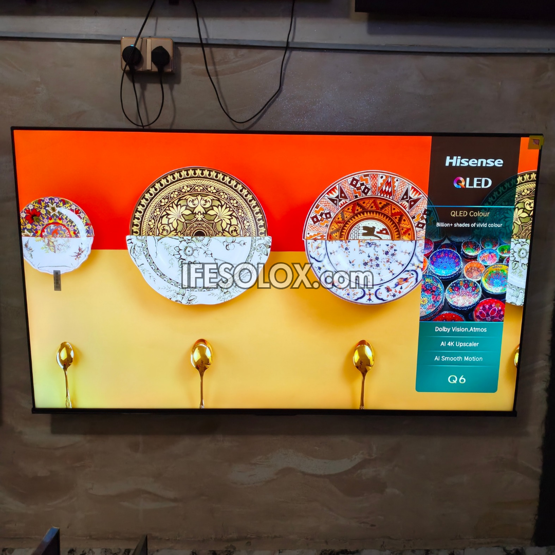 A Hisense OLED TV mounted on a textured wall, displaying a colorful screen with decorative plates and gold spoons. The Hisense and QLED branding is visible on the screen.