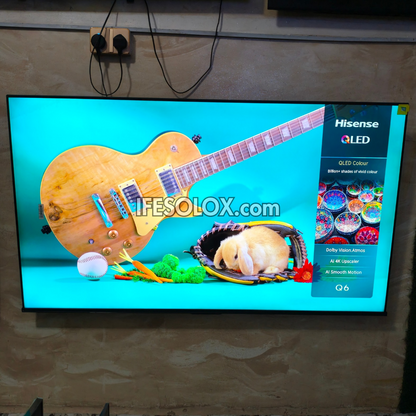 A Hisense QLED TV mounted on a textured wall, displaying a vibrant image with a large wooden guitar, a sleeping rabbit in a basket, and a bright cyan background. The Hisense QLED logo is visible on the screen's right side.