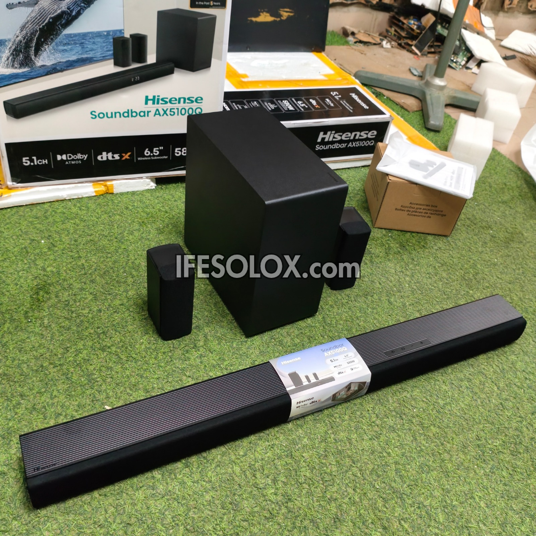 Hisense Soundbar AX5100Q 5.1 channel home theater speaker system with a long bar, a subwoofer, and two satellite speakers, displayed on green artificial grass with product boxes in the background.