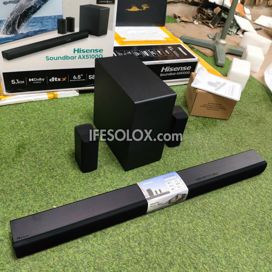 Hisense Soundbar AX5100Q 5.1 channel home theater speaker system with a long bar, a subwoofer, and two satellite speakers, displayed on green artificial grass with product boxes in the background.