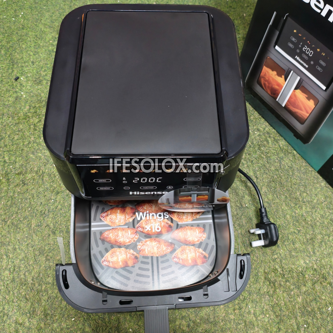 A black Hisense air fryer with the lower basket open, showing cooked chicken wings inside. The product is placed on a green artificial grass surface, with a second air fryer and its power cord visible in the background.