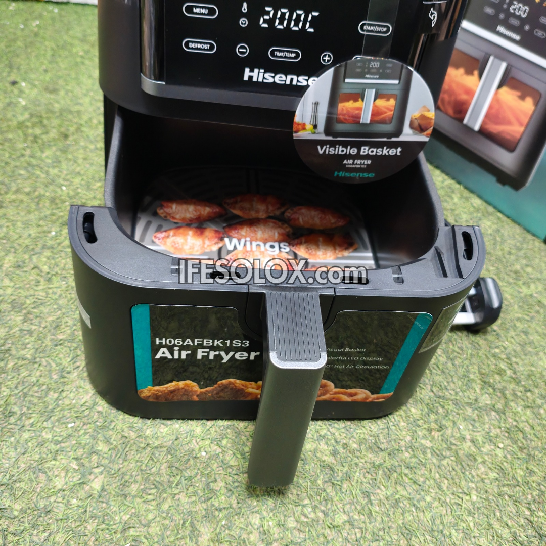 Hisense air fryer with the basket pulled out, showing cooked chicken wings inside, set on a green grass-like surface. The digital display at the top reads 200, and a circular inset highlights the visible basket.