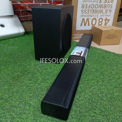 Black soundbar and subwoofer on a grassy surface with visible branding and website.