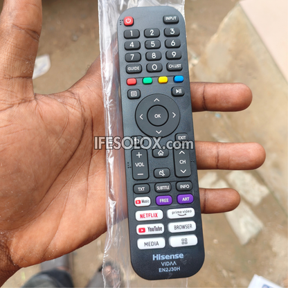 A Hisense VODA EN230H TV remote control, still in its clear plastic protective sleeve, held in a person's hand. The remote is black with various colored buttons including red, green, yellow, blue, and purple, and features built-in app icons for Netflix, YouTube, Spotify, and others.