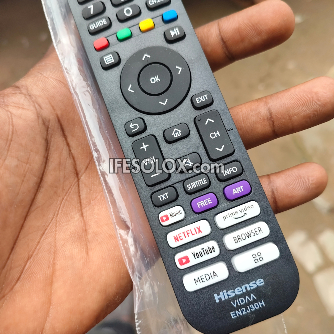 A close-up of a Hisense TV remote control held in a hand, still partially in its clear plastic packaging. The remote has black buttons with white icons and colorful accent buttons for navigation, media, and streaming services including Netflix, YouTube, Amazon Prime Video, and BROWSER.