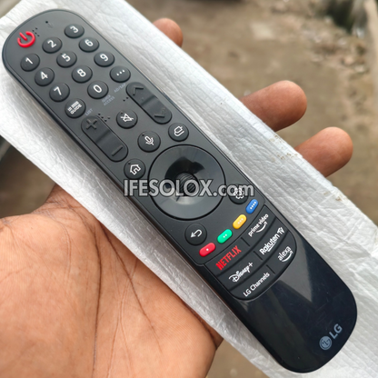 An LG smart TV remote control held in a person's hand, wrapped in white protective foam. The remote is black with white icons and features buttons for numbers, navigation, power, and popular app logos including Netflix, Disney+, and YouTube.
