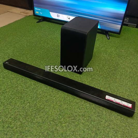 Black soundbar and subwoofer on a green carpet with a TV in the background.