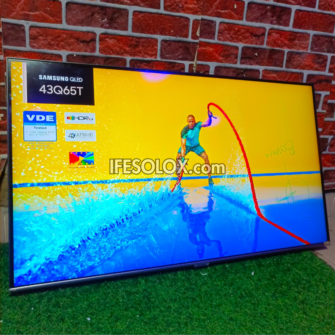 Samsung QLED TV displaying a sports scene with branding and website text on a brick wall background.
