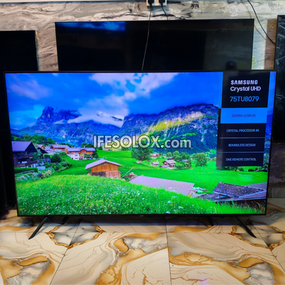 Samsung Crystal UHD 75TU8079 television displaying a colorful mountain landscape, set on a marble-patterned floor in a showroom.