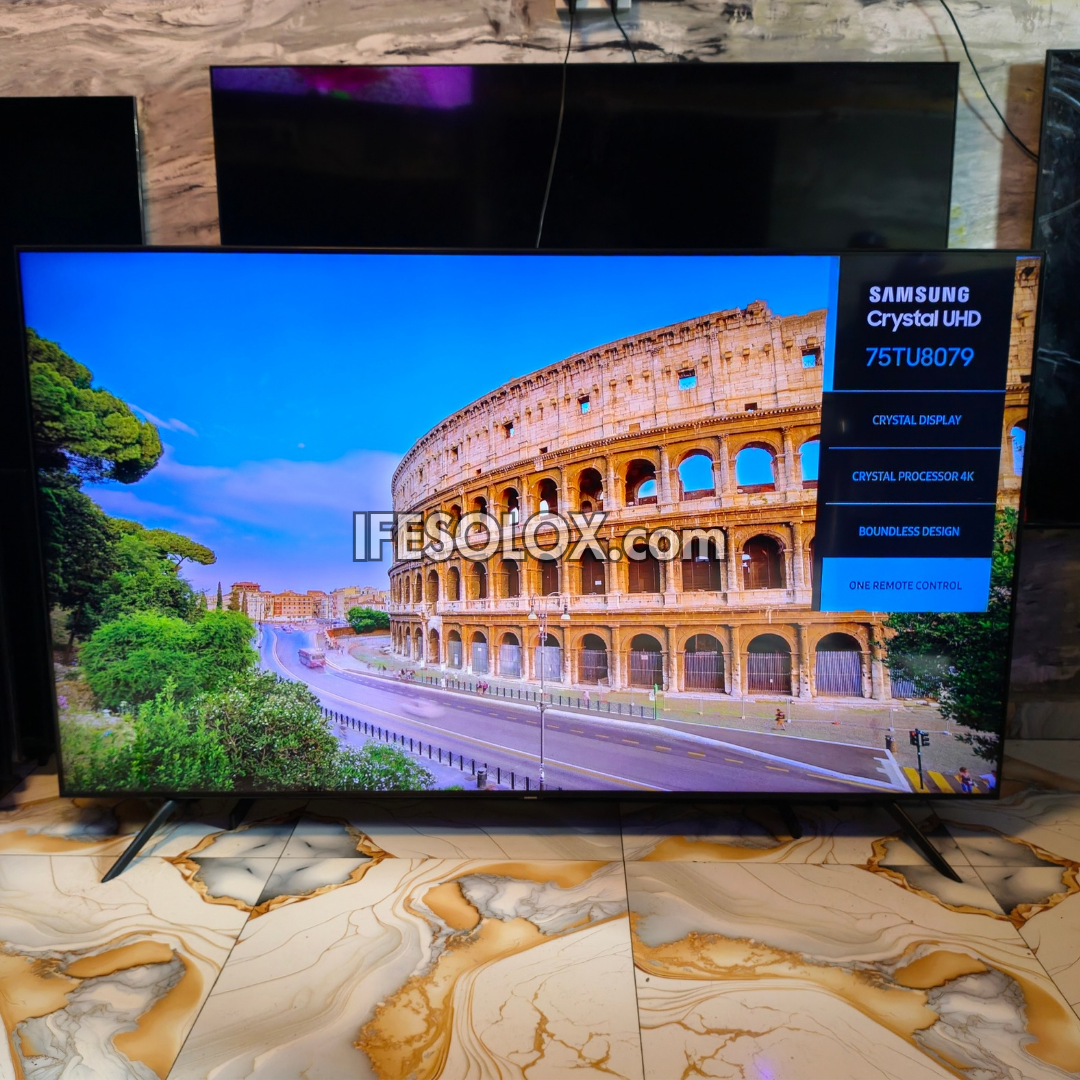 A Samsung Crystal UHD 75TU8079 television displaying the Colosseum in Rome on its screen, set against a stone-tiled wall and marble-patterned floor.