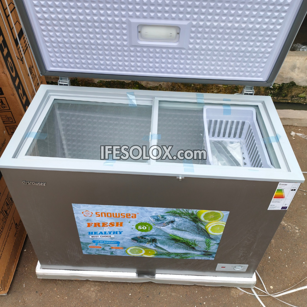 A Snowsea chest freezer with a gray exterior, white lid interior, and clear glass top, shown with the lid open. A large 'IFESOLOX.