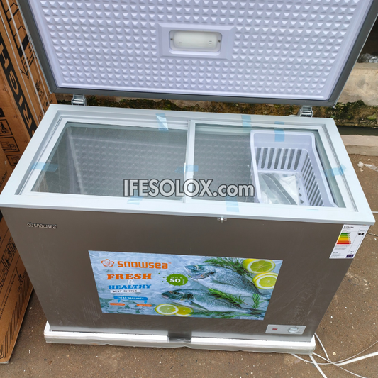 A Snowsea chest freezer with a gray exterior, white lid interior, and clear glass top, shown with the lid open. A large 'IFESOLOX.