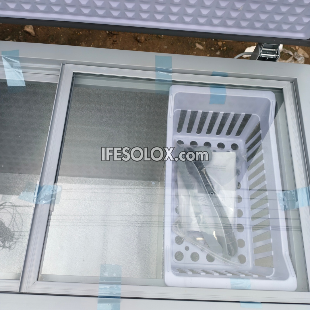 A white plastic storage basket with ventilation slots and drainage holes, shown inside a sliding glass compartment of a white metal cabinet. The basket is secured with blue tape, and a watermark 'IFESOLOX.