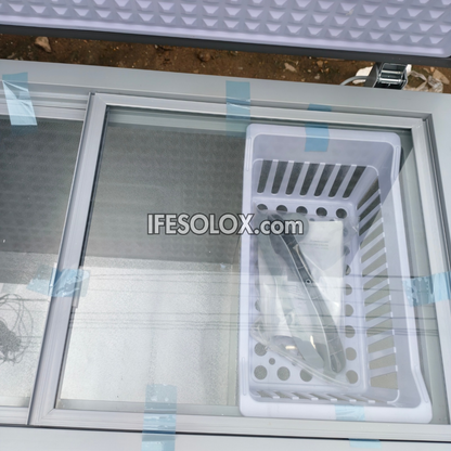 A white plastic storage basket with ventilation slots and drainage holes, shown inside a sliding glass compartment of a white metal cabinet. The basket is secured with blue tape, and a watermark 'IFESOLOX.