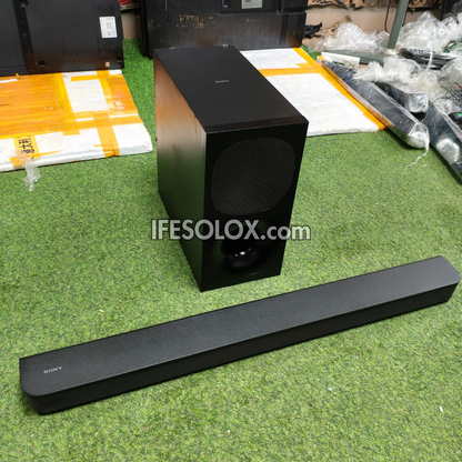 Sony soundbar and matching subwoofer on a green artificial turf surface, with shipping boxes and packaged items in the background. A 'IFESOLOX.