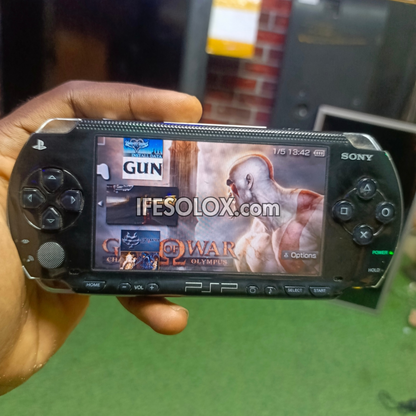 Hand holding a Sony PlayStation Portable (PSP) with God of War game selection on screen