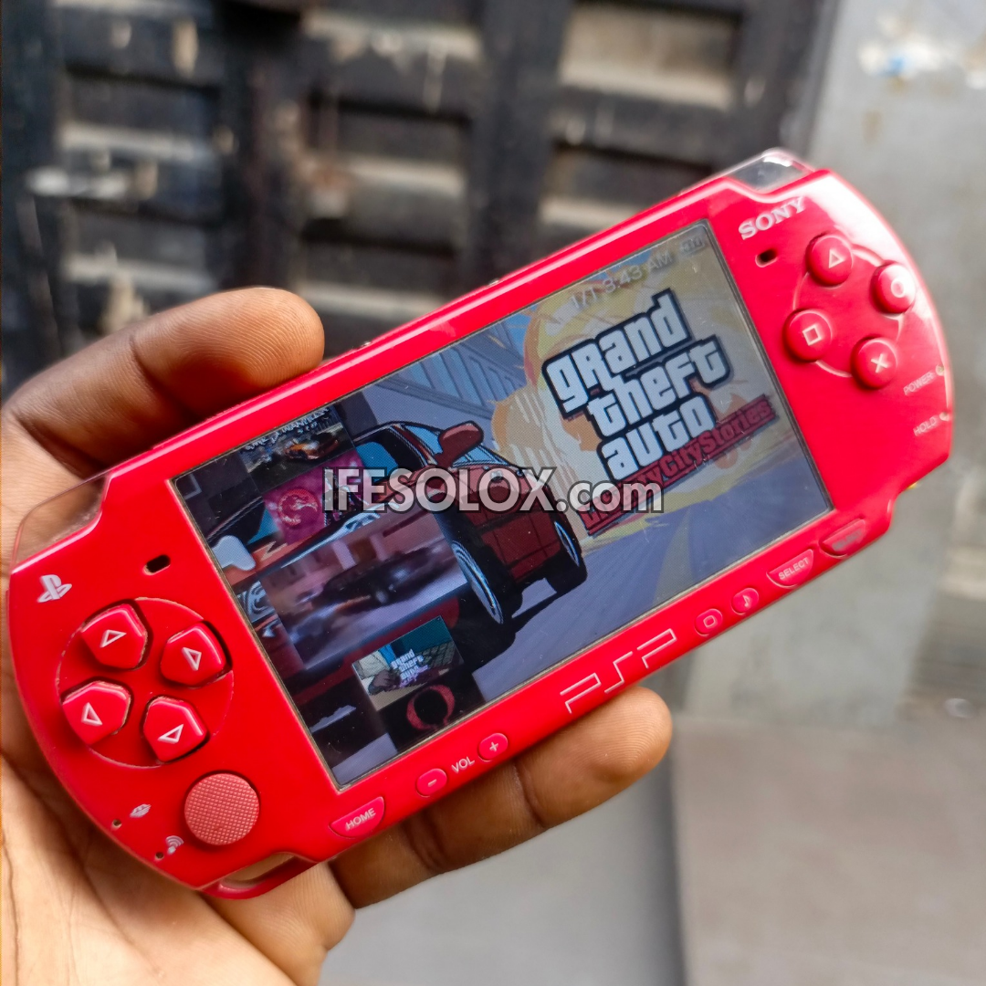 Red Sony portable gaming device displaying 'Grand Theft Auto' game on a blurred background
