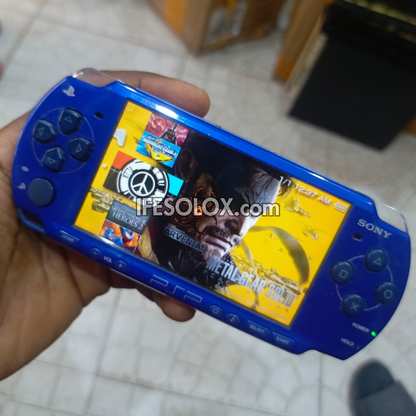 Blue Sony PSP handheld gaming console with a colorful display held by a hand.